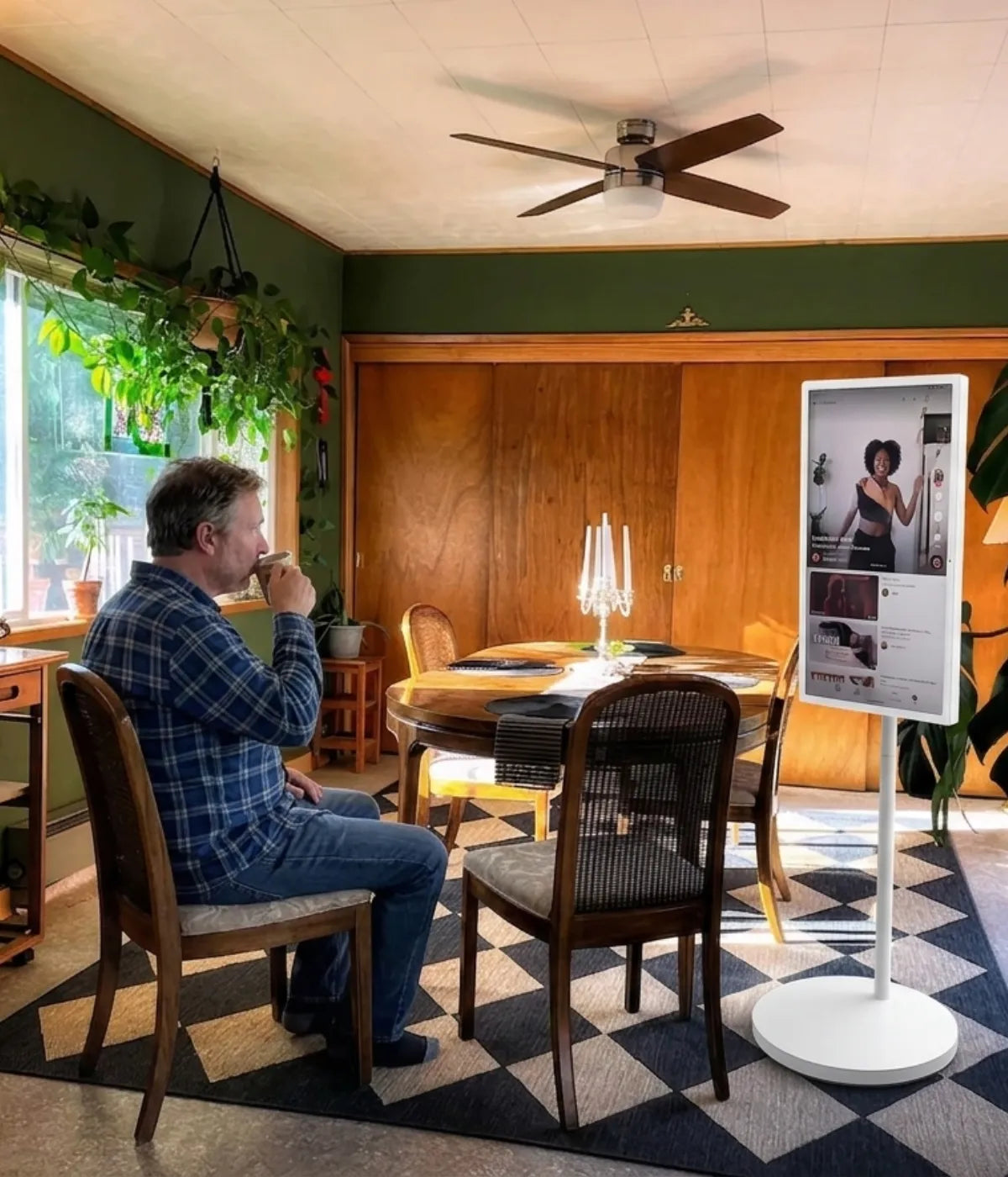 A man is sitting at the dining table having coffee, with his GFF portable TV on wheels playing short videos nearby